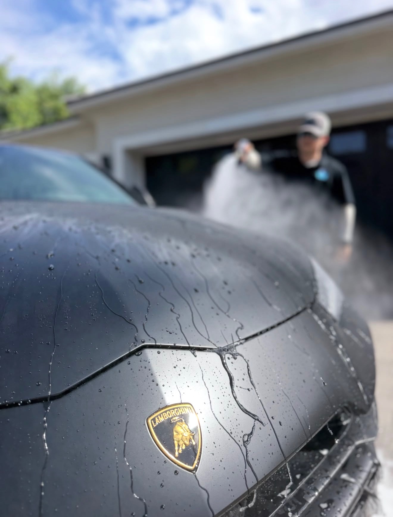 Shark Shine detailer rinsing a matte black Lamborghini in an Arizona driveway
